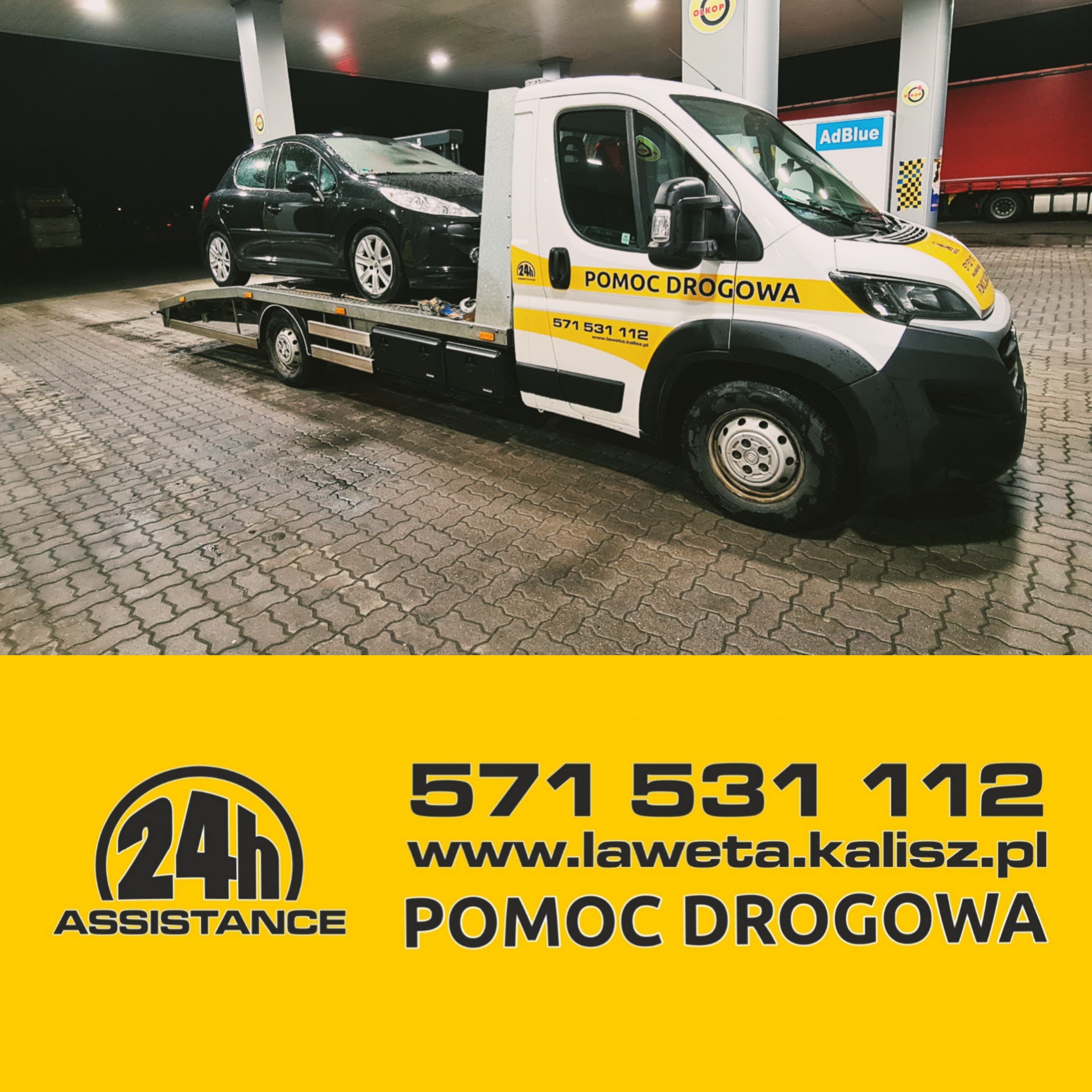 Laweta z czarnym samochodem osobowym na platformie, stojąca na stacji benzynowej z widocznym logo 'Pomoc Drogowa' i danymi kontaktowymi na pojeździe.