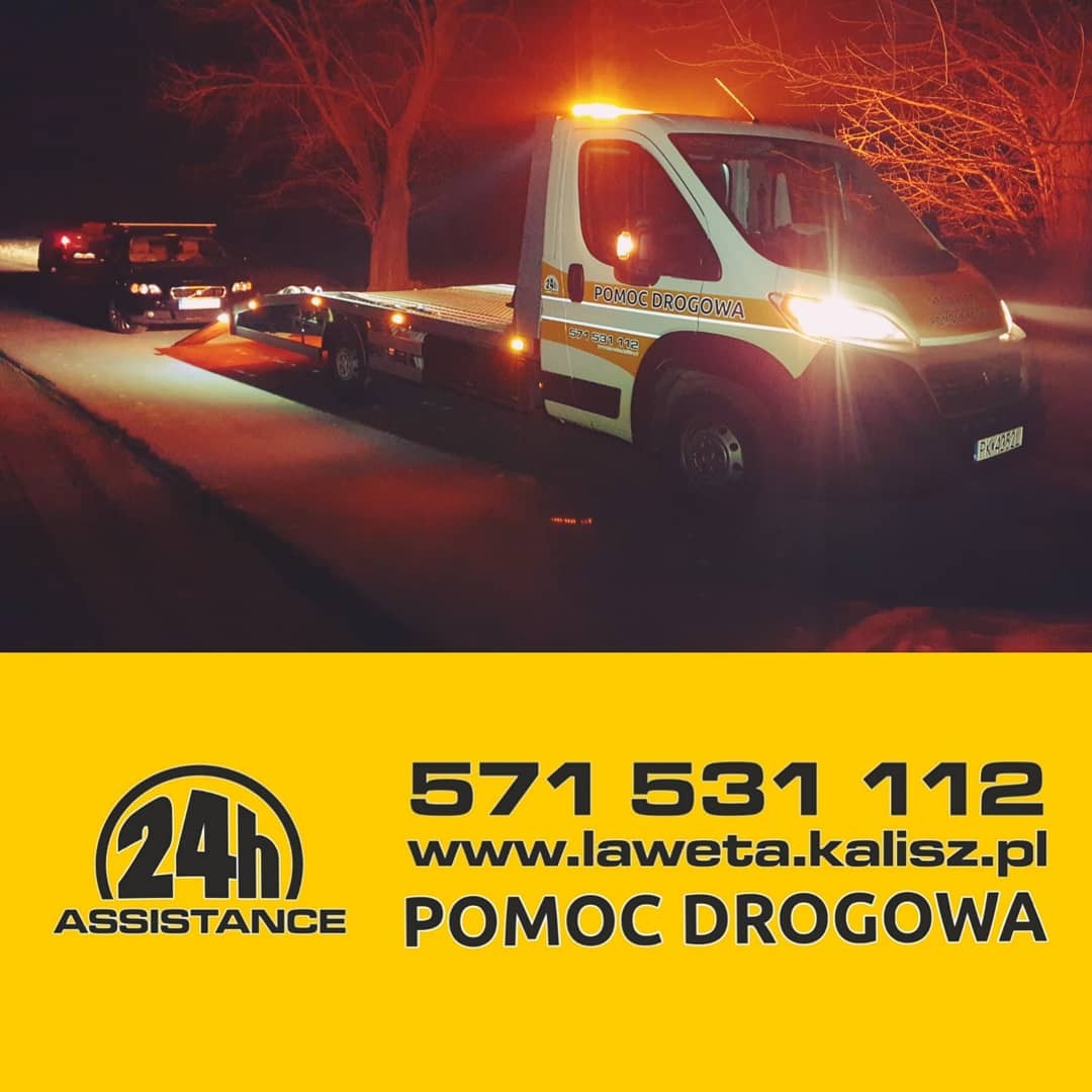 Nocna akcja pomocy drogowej: biała laweta z włączonymi światłami awaryjnymi, wciąga uszkodzony samochód na platformę, oświetlona droga w zimowej scenerii.