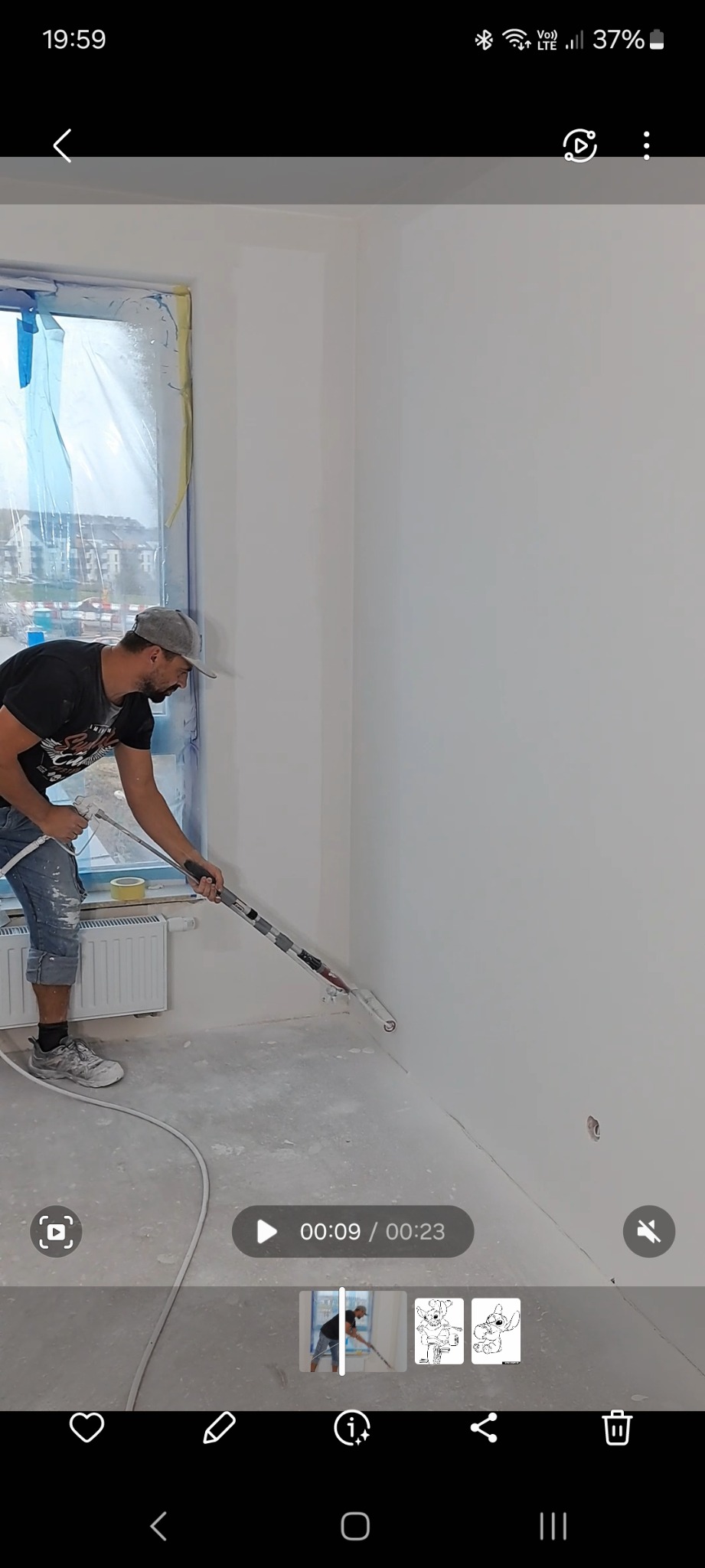 Mężczyzna w czarnej koszulce i jeansach szpachluje ścianę przy użyciu agregatu natryskowego, okno zabezpieczone folią, widoczne ślady szpachli na podłodze.