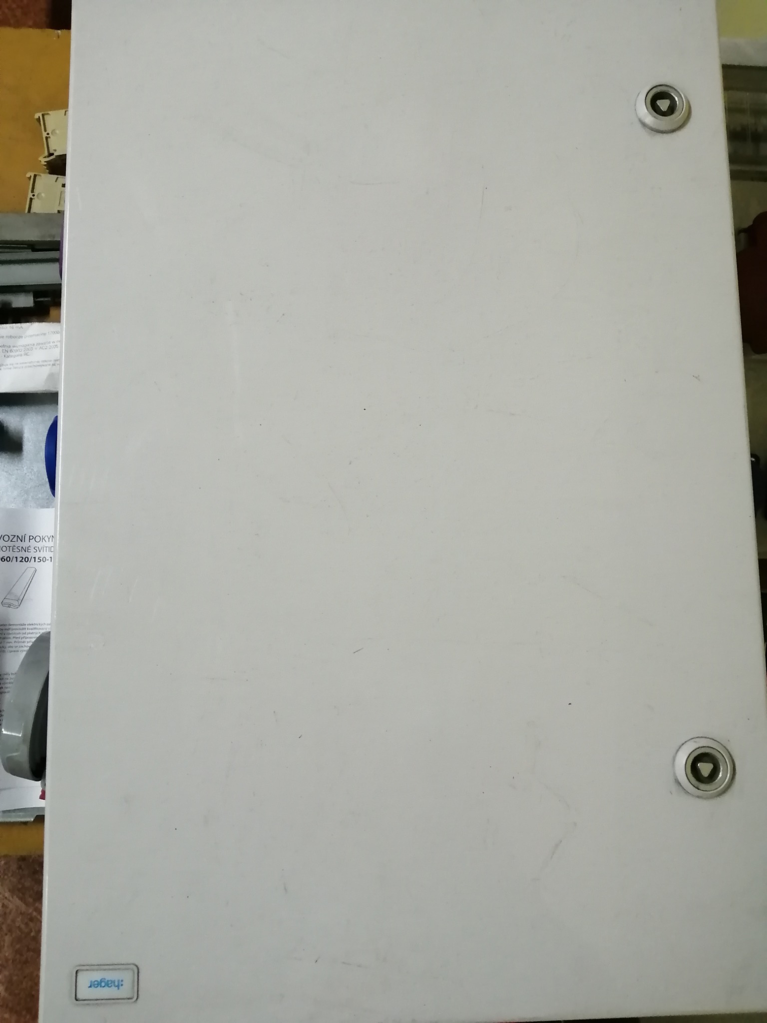 Zamknięta, szara skrzynka elektryczna Hager z dwoma zamkami na jasnym tle, widoczna etykieta z instrukcjami po lewej stronie.