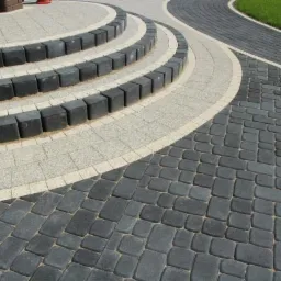 Kaskadowe schody z ciemnej kostki brukowej z jasnymi elementami dekoracyjnymi, prowadzące do trawnika