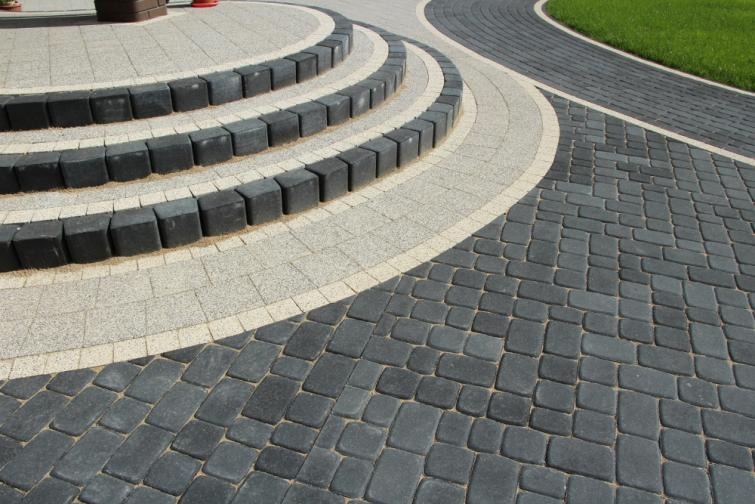 Kaskadowe schody z ciemnej kostki brukowej z jasnymi elementami dekoracyjnymi, prowadzące do trawnika