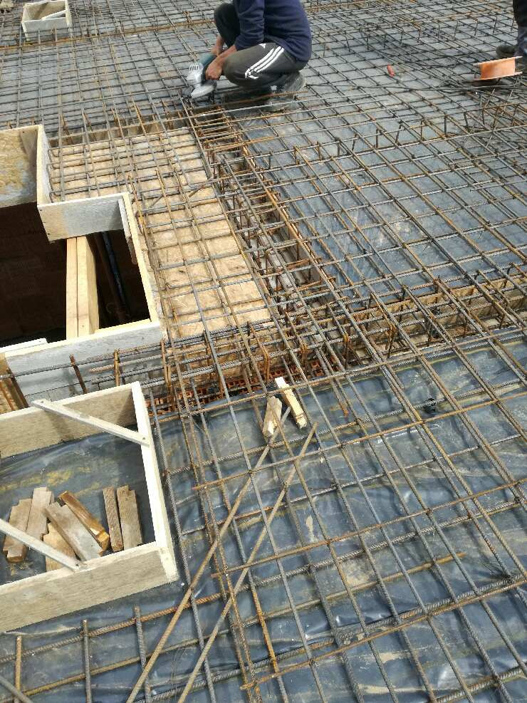 Zbrojenie fundamentu z siatki stalowej na folii, widoczny pracownik w trakcie pracy i drewniane szalunki.
