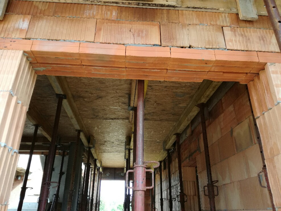 Wnętrze budowanego domu z pustaków ceramicznych Porotherm, widoczne stropy podparte stemplami budowlanymi i fragmenty ścian. Widoczny otwór drzwiowy z nadprożem.