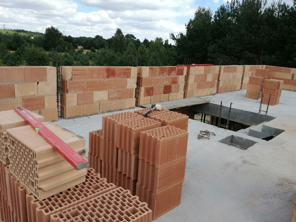 Wznoszenie ścian z bloczków ceramicznych na stropie budynku w stanie surowym otwartym, widoczne zbrojenia i poziomica na palecie bloczków.