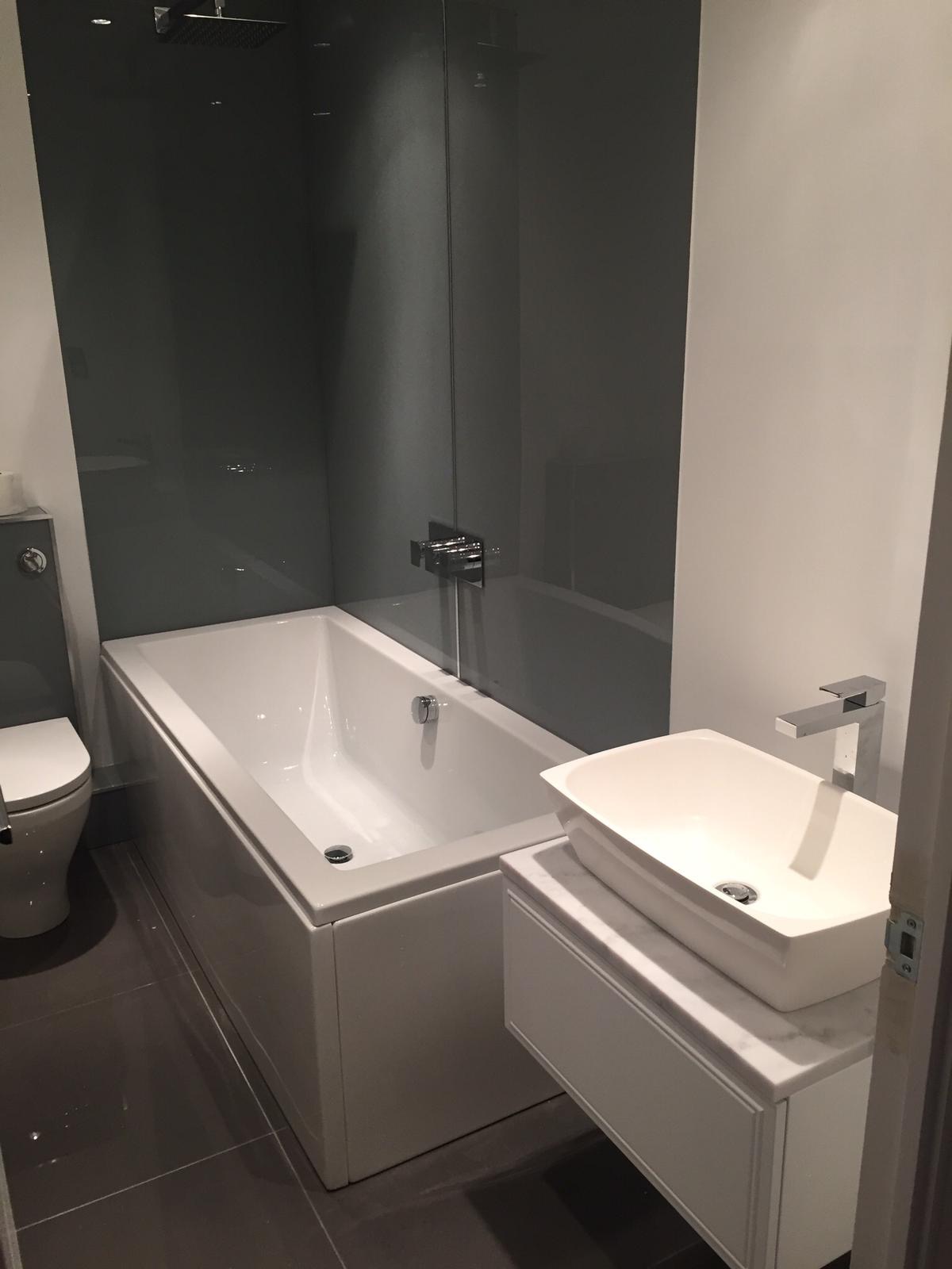 Nowoczesna łazienka z białą prostokątną wanną zabudowaną, umywalką nablatową na szafce z marmurowym blatem i szarą ścianą prysznicową ze szkła.