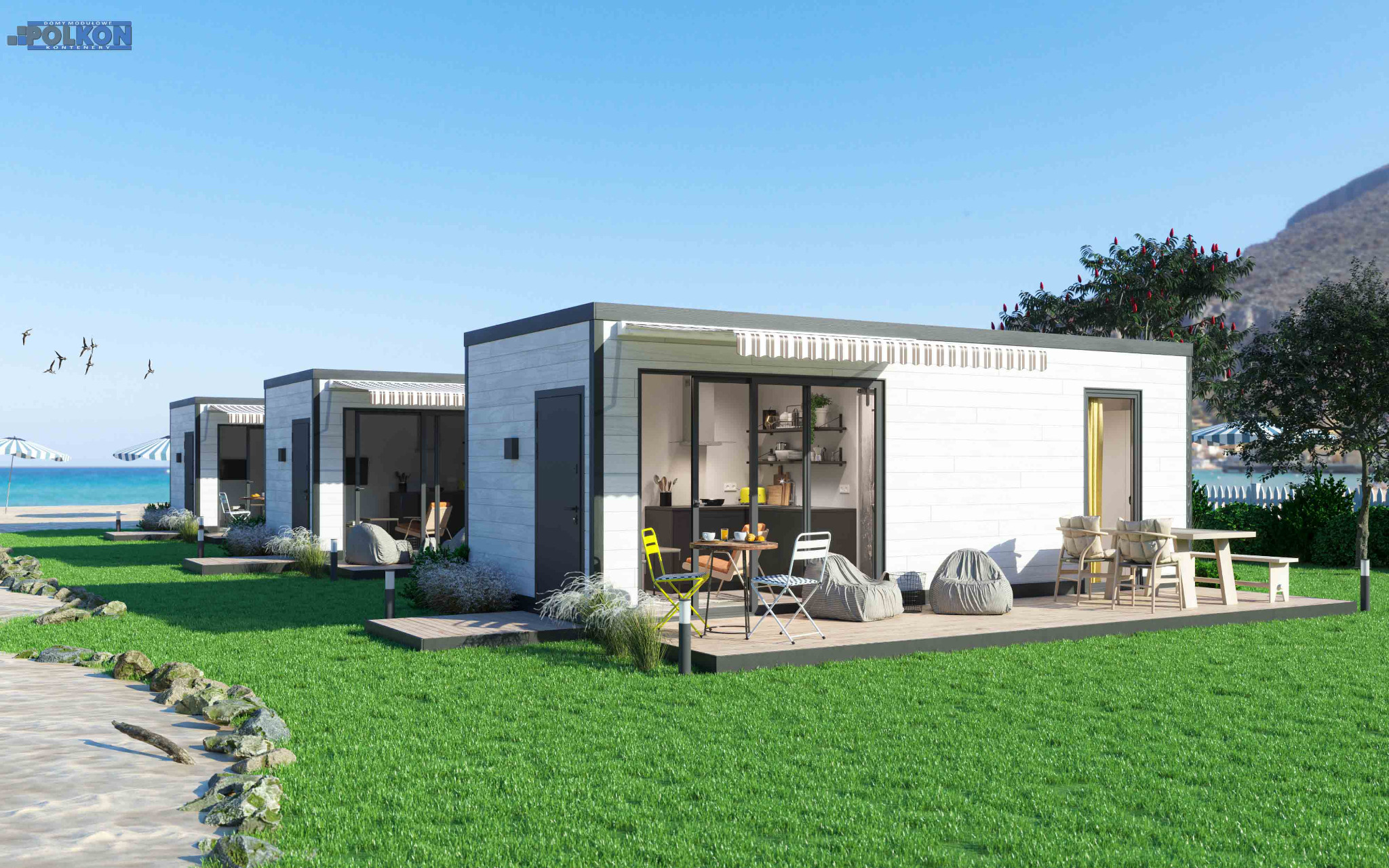 Rząd nowoczesnych domów modułowych z białymi elewacjami i szarymi akcentami, każdy z tarasem wyposażonym w meble ogrodowe, zlokalizowanych na zielonym trawniku przy plaży z widokiem na morze i góry...