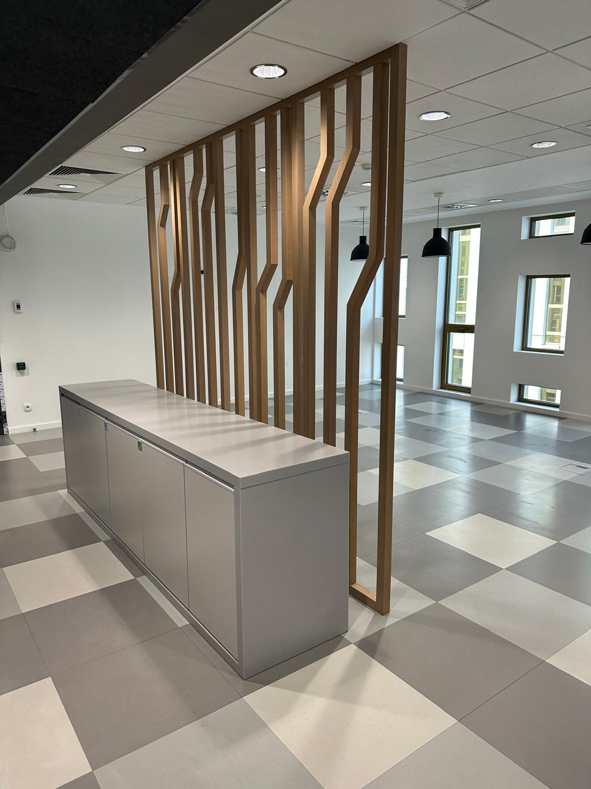 Nowoczesne biuro z szaro-białą szachownicą na podłodze, drewnianą ścianką działową i szarą zabudową meblową.