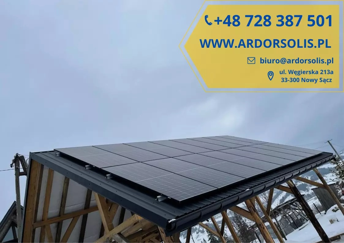 Panel słoneczny na dachu budynku gospodarczego w zimowej scenerii, z widocznym banerem reklamowym firmy.