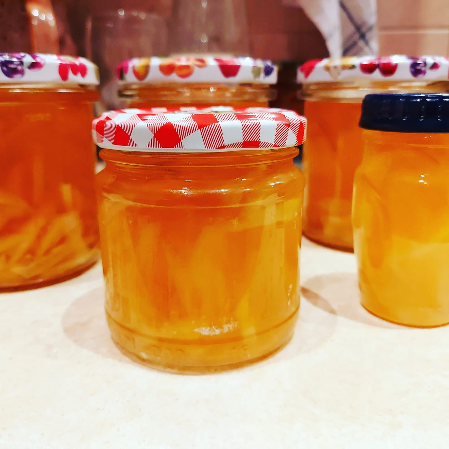 Rząd słoików z domową konfiturą cytrynową, z różnymi wzorami na zakrętkach, stojących na blacie.