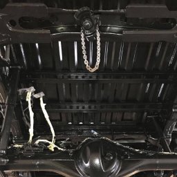 JD Garage - Spód samochodu po zabezpieczeniu antykorozyjnym, widoczne elementy zawieszenia i podwozia pokryte czarną, błyszczącą powłoką, łańcuch podtrzymujący element konstrukcyjny.