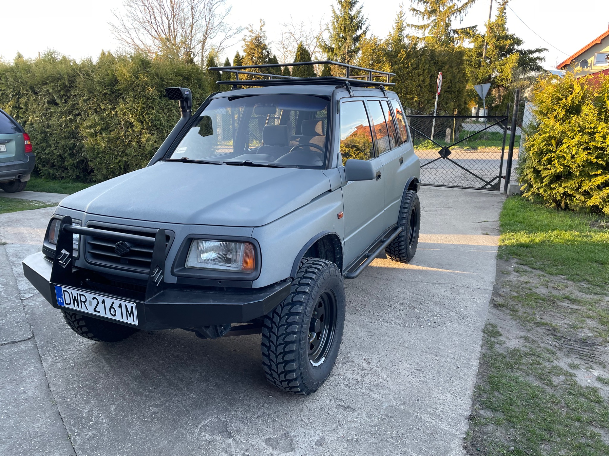 Szary Suzuki Vitara po tuningu off-roadowym: snorkel, bagażnik dachowy, opony terenowe, stalowy zderzak przedni z tablicą rejestracyjną DWR 2161M.