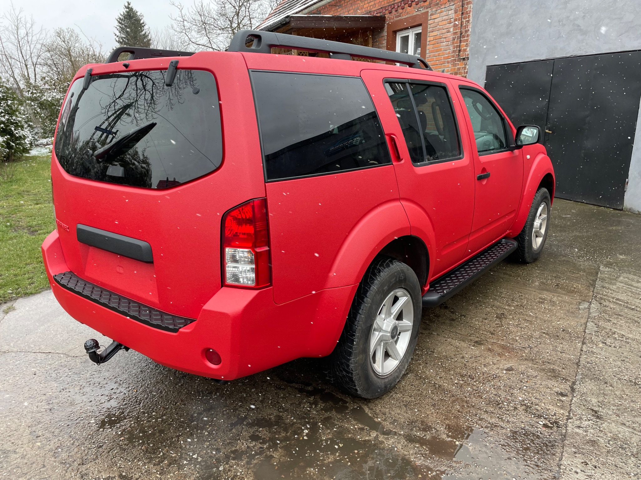 Czerwony SUV po nałożeniu matowej powłoki ochronnej, widok z tyłu na tle budynku i padającego śniegu.