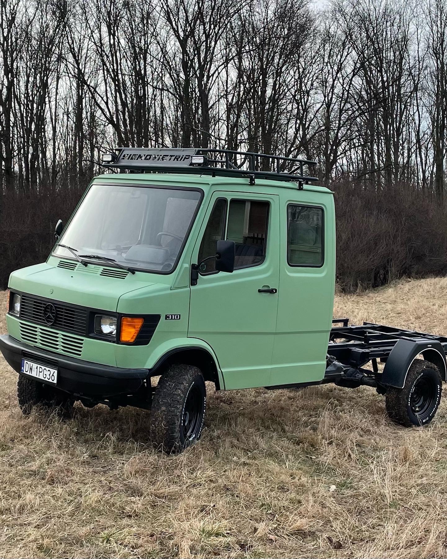 Odrestaurowany Mercedes-Benz 310 w pastelowej zieleni, z czarnym orurowaniem i bagażnikiem dachowym z napisem 'SIEMOWITRIP', bez zabudowy skrzyniowej, na tle jesiennego krajobrazu.