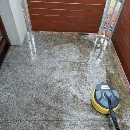 Czyszczenie kamiennej posadzki na balkonie przy użyciu szorowarki Karcher, widoczne mokre ślady po czyszczeniu i drewniane panele balkonowe.