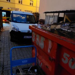 R.M.K Cleaning Service - Czerwony kontener na gruz wypełniony odpadami budowlanymi, częściowo zasłaniający biały samochód dostawczy z numerem rejestracyjnym WA-7972, w tle budynek mieszkalny z oknami.