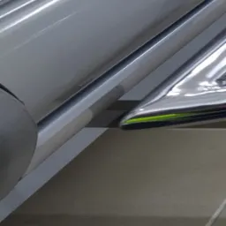 Fragment metalowej konstrukcji schodów lub balustrady z elementami nierdzewnymi i zielonym akcentem, widok z dołu, słabe oświetlenie.