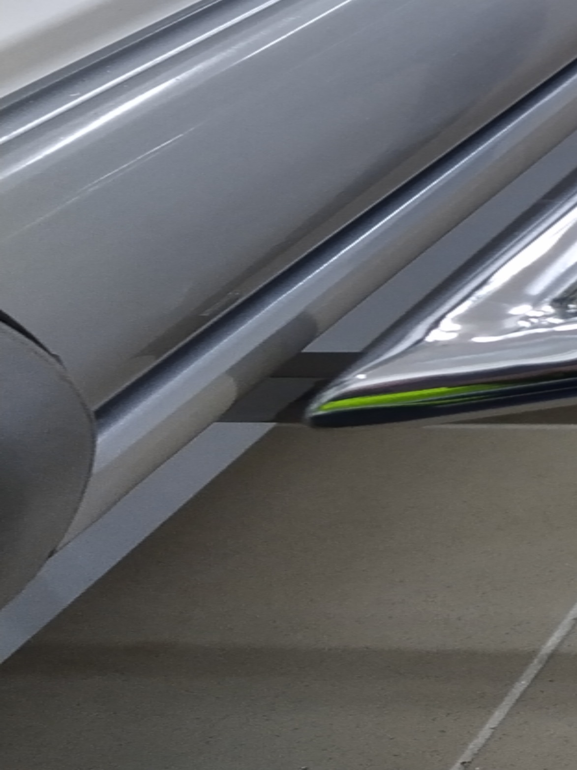 Fragment metalowej konstrukcji schodów lub balustrady z elementami nierdzewnymi i zielonym akcentem, widok z dołu, słabe oświetlenie.