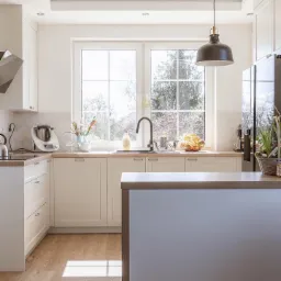 Jasna kuchnia na wymiar w Koszalinie z drewnianym blatem, wyspą kuchenną i dużym oknem z widokiem na drzewa.