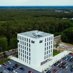 Moonphase Studio - Biały, nowoczesny budynek biurowy z logo firmy na elewacji, otoczony parkingiem i lasem, widok z lotu ptaka.