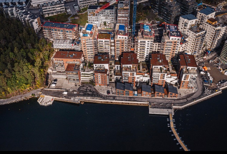 Widok z lotu ptaka na nowoczesne osiedle mieszkaniowe nad wodą, z budynkami o różnej wysokości i architekturze, częściowo w trakcie budowy, z dźwigiem w tle.