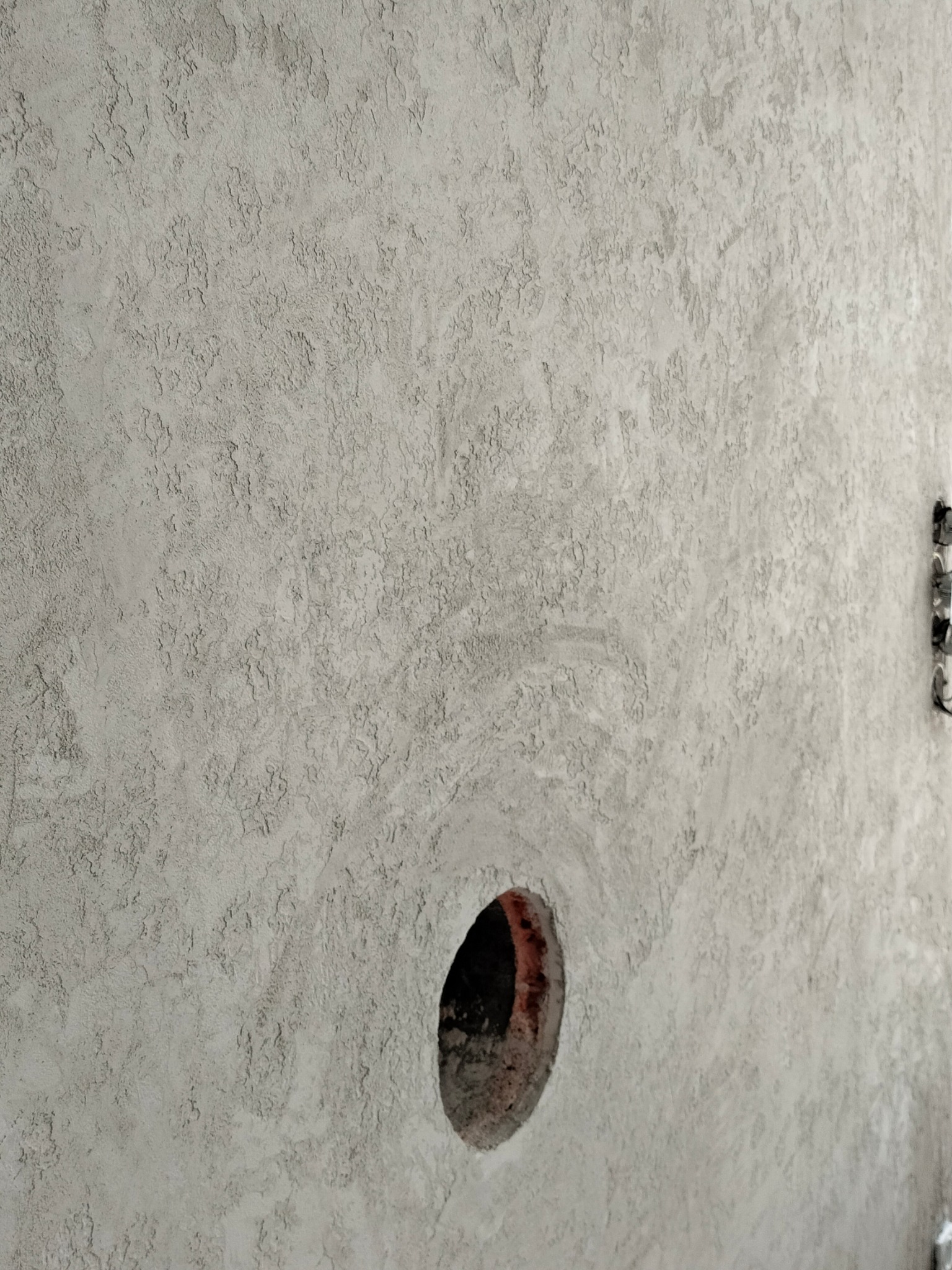 Szara ściana z fakturą i otworem na instalację elektryczną, widoczne kable.