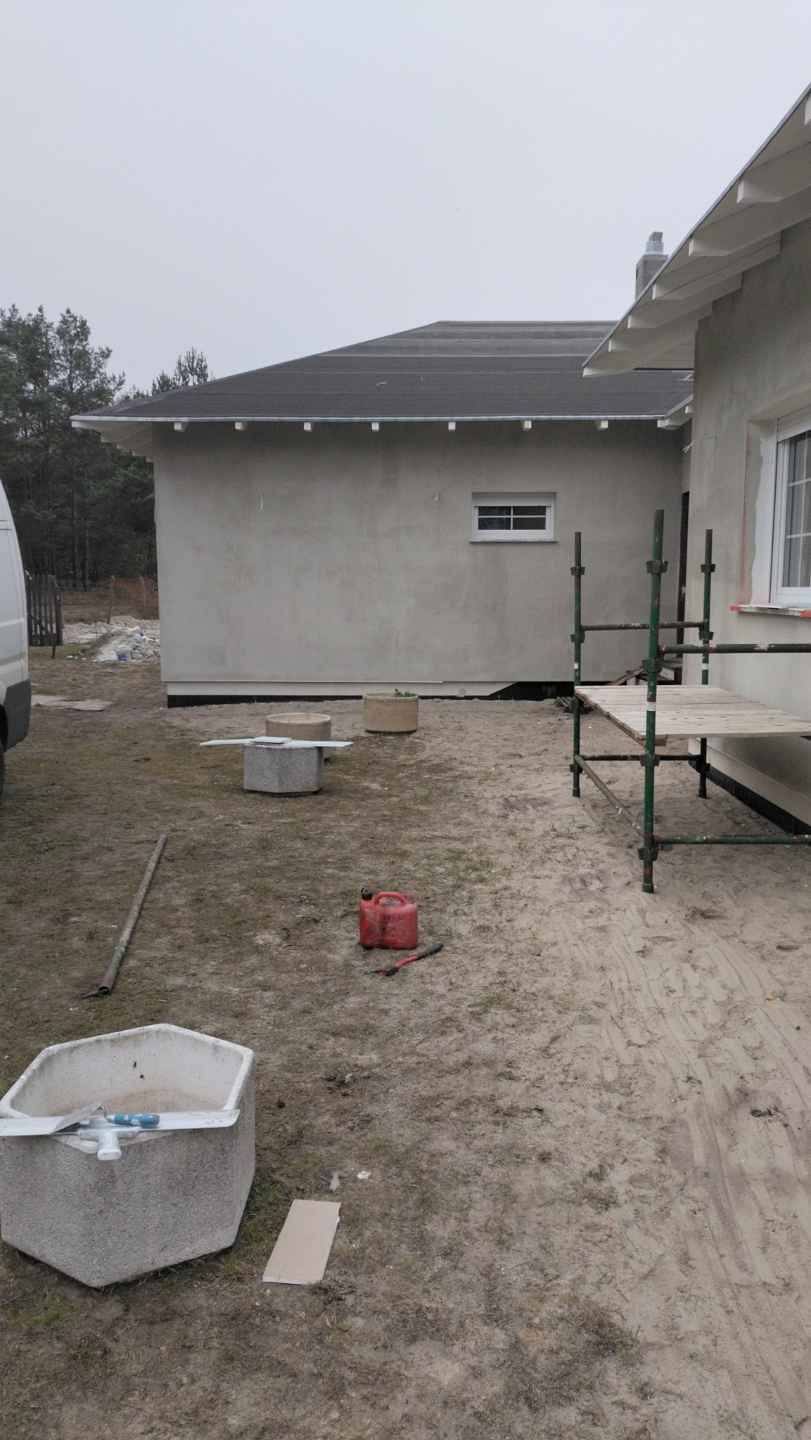 Budynek po nałożeniu tynku zewnętrznego, widoczne rusztowanie, pojemnik z narzędziami, kanister i fragment samochodu dostawczego.