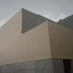 Budynek przemysłowy z blachy trapezowej w kolorze beżowym, widoczny dźwig na tle pochmurnego nieba.