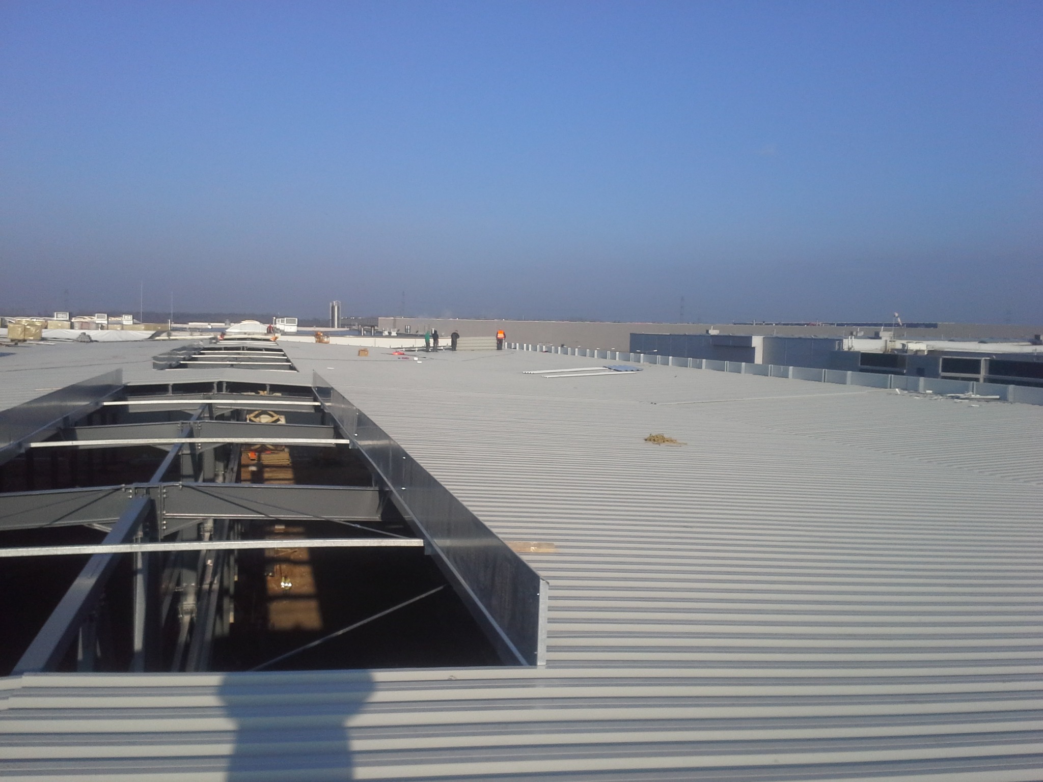 Montaż konstrukcji stalowej na dachu przemysłowym z blachy trapezowej, widoczni pracownicy w oddali.