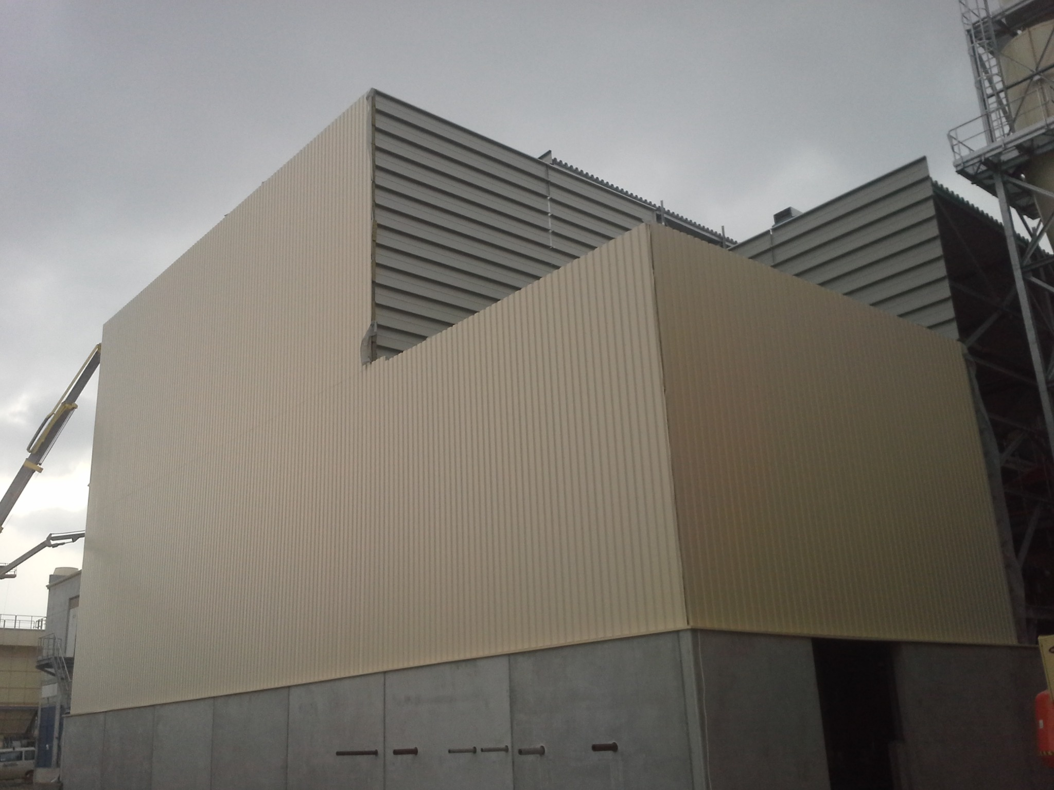 Budynek przemysłowy z blachy trapezowej w kolorze beżowym, widoczny dźwig na tle pochmurnego nieba.