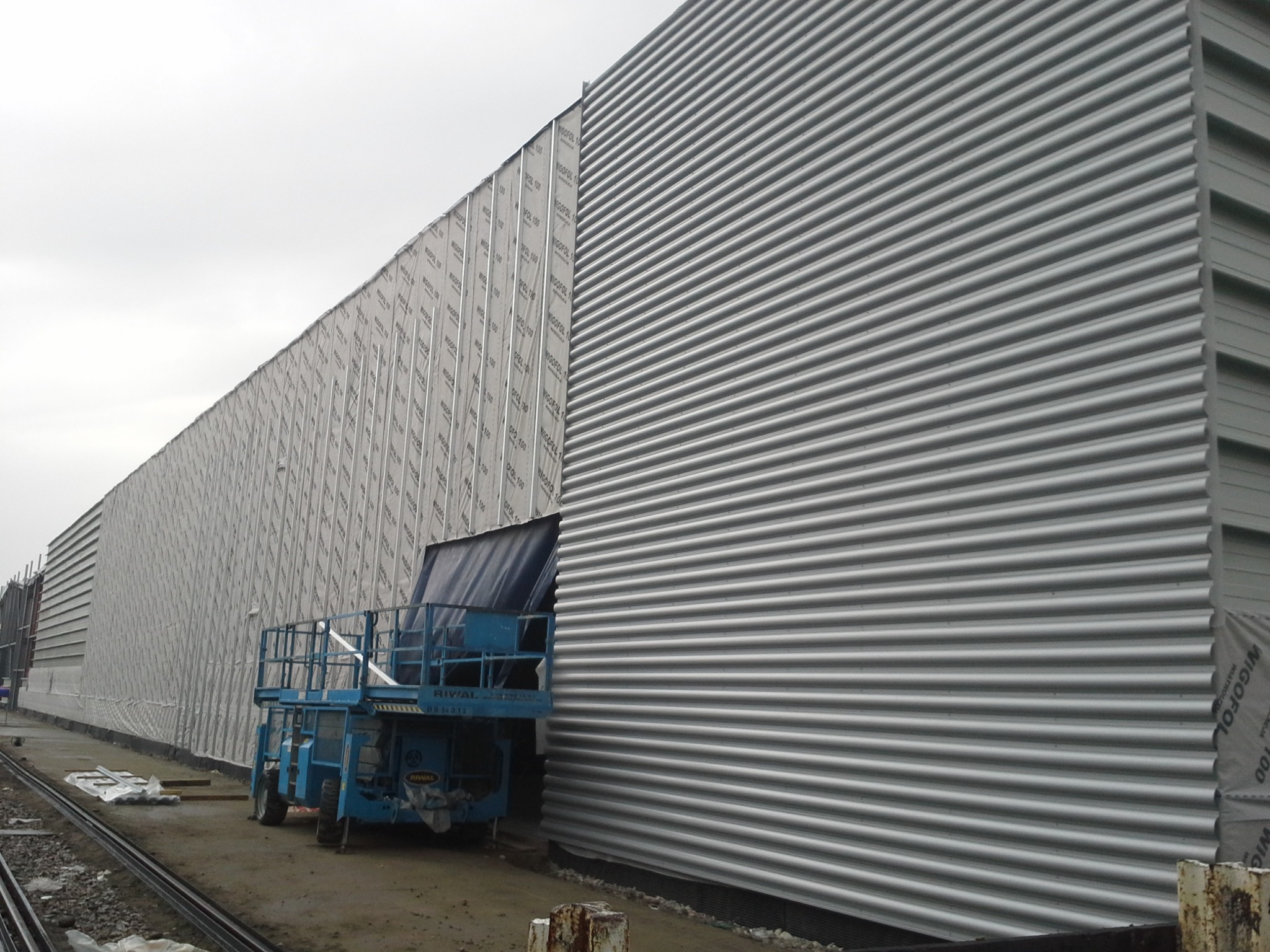 Montaż elewacji przemysłowej z blachy trapezowej, widoczna podnośnik koszowy i folia izolacyjna Wigofol 100.