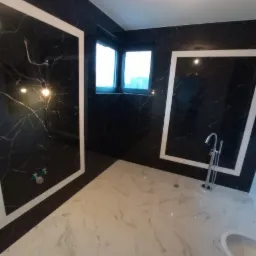 Wykończona łazienka z czarnymi ścianami imitującymi marmur, białymi fugami i białą marmurową podłogą, wolnostojąca bateria wannowa i bidet.