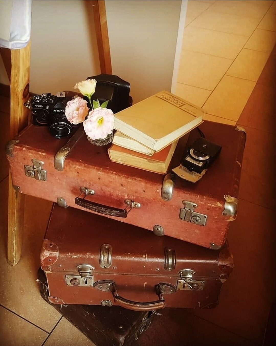 Dekoracja weselna w stylu vintage: ułożone stare walizki, na nich aparat fotograficzny Zenit, kwiaty w małym wazonie i książki z lat 60.