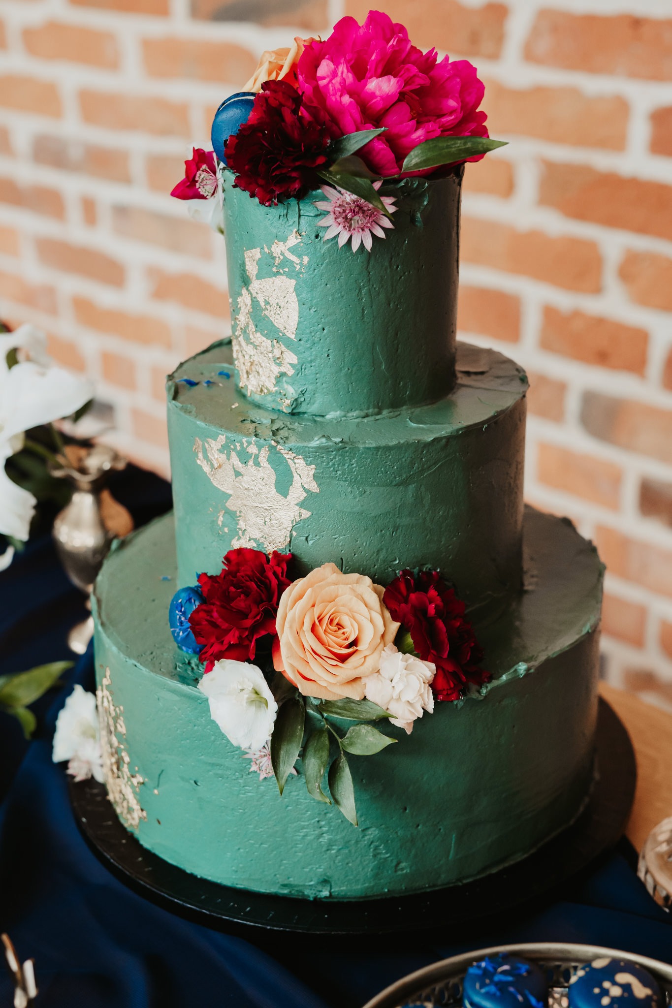 Trzypiętrowy tort weselny w odcieniach zieleni z dekoracją ze złota i kwiatów w kolorach różu, czerwieni i bieli, wykonany w Warszawie.