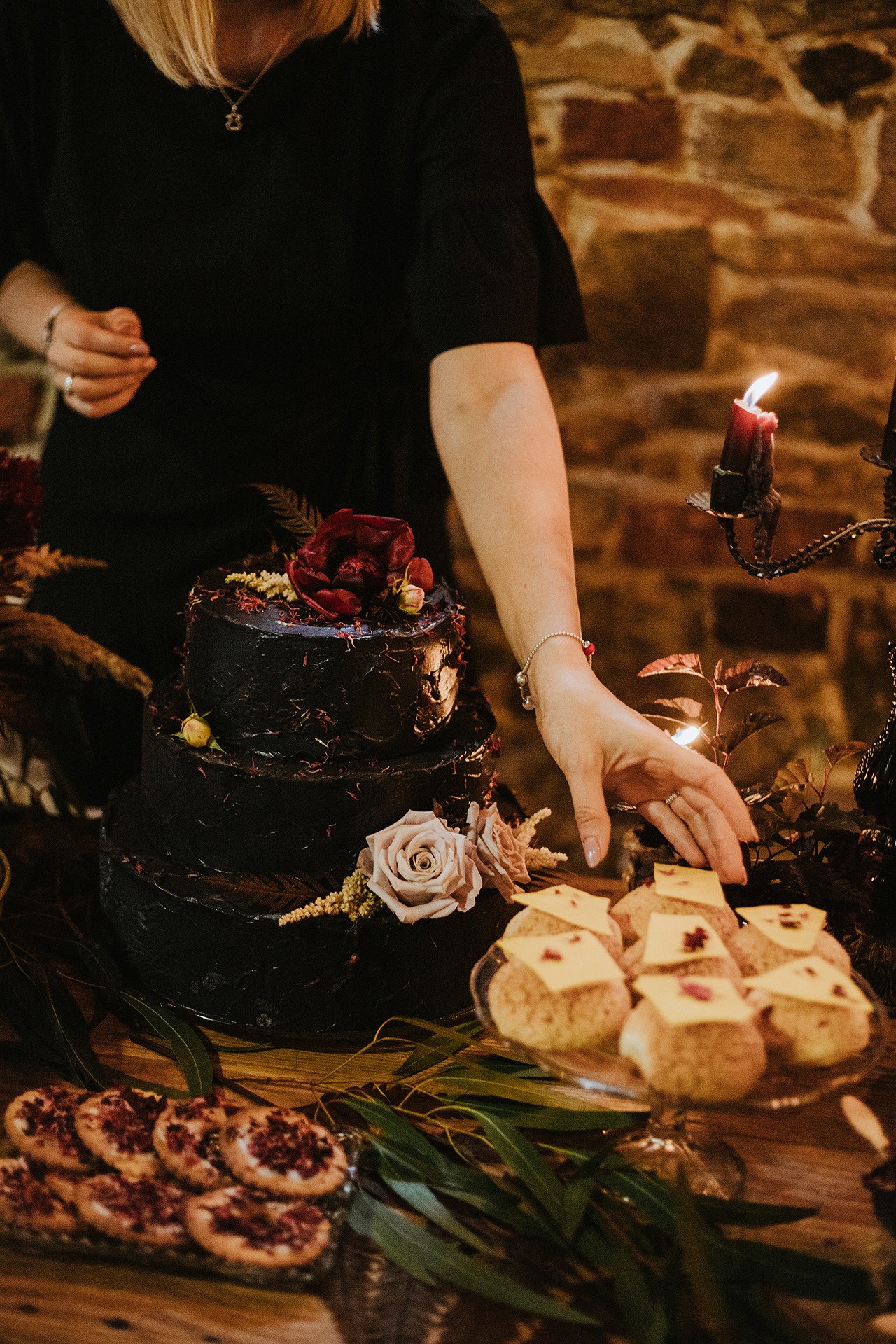 Stylizowany stół z ciemnym tortem, ciastkami i płonącymi świecami w kandelabrze, aranżacja w klimacie mrocznego zamku.