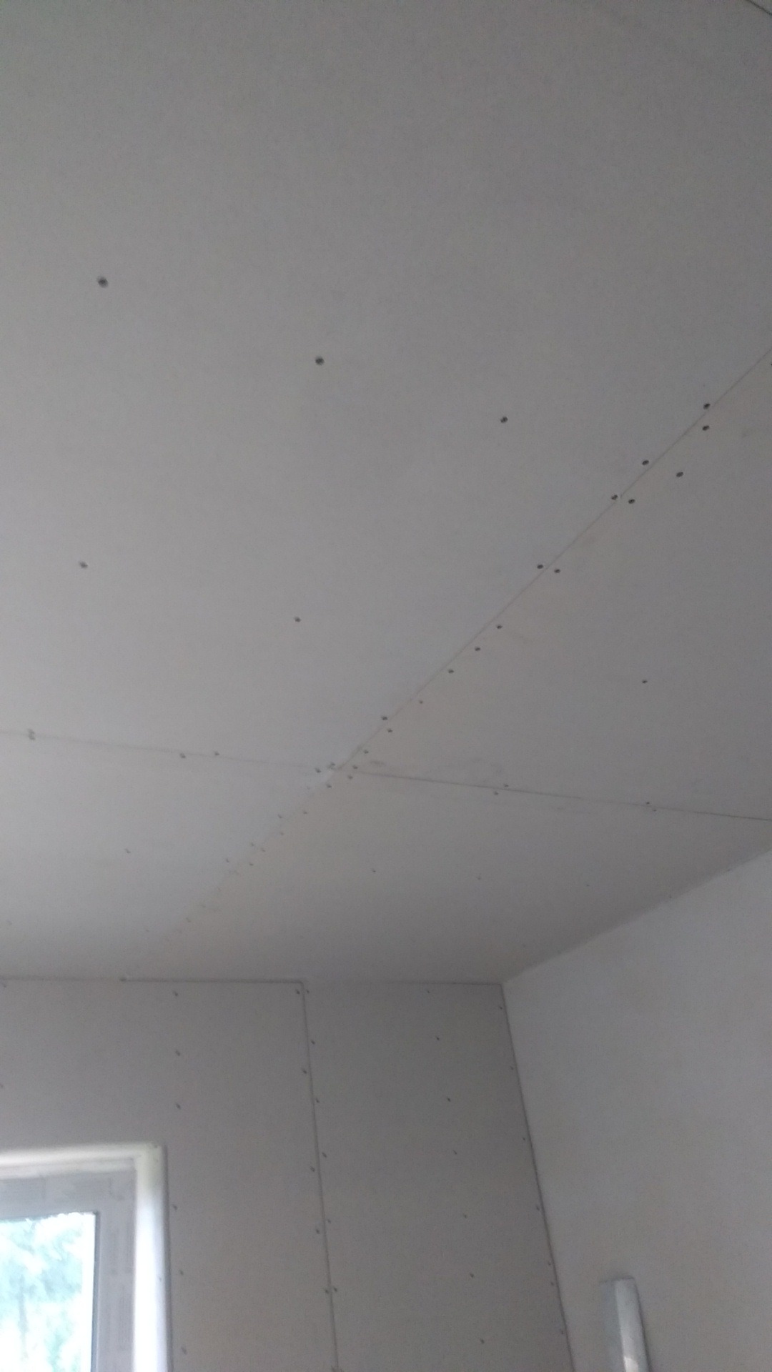 Sufit i ściany w trakcie montażu płyt kartonowo-gipsowych, widoczne łączenia i wkręty, surowe wykończenie, okno w lewym dolnym rogu.