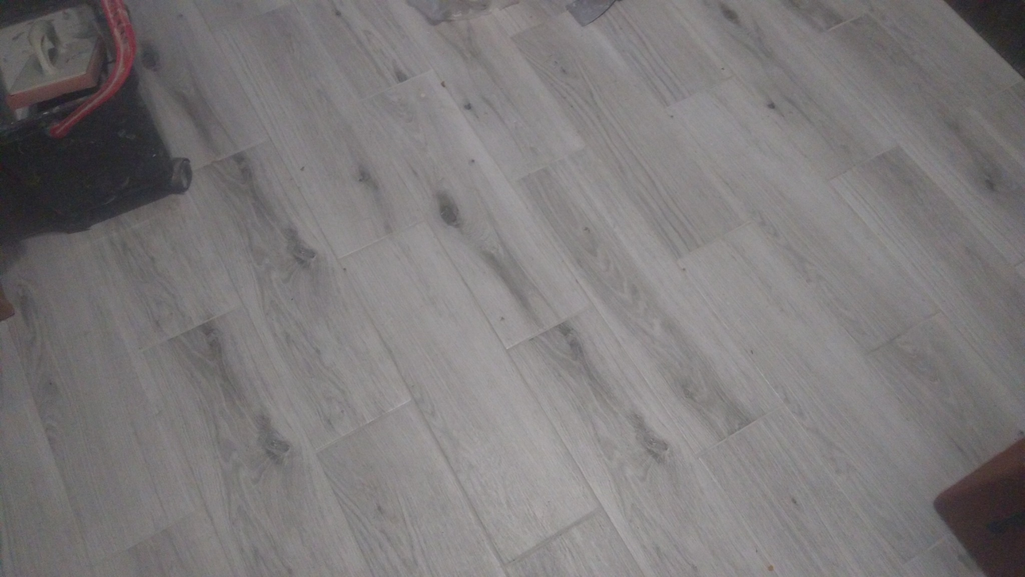 Ułożone panele podłogowe w odcieniach szarości z widocznymi narzędziami pracy w rogu kadru.