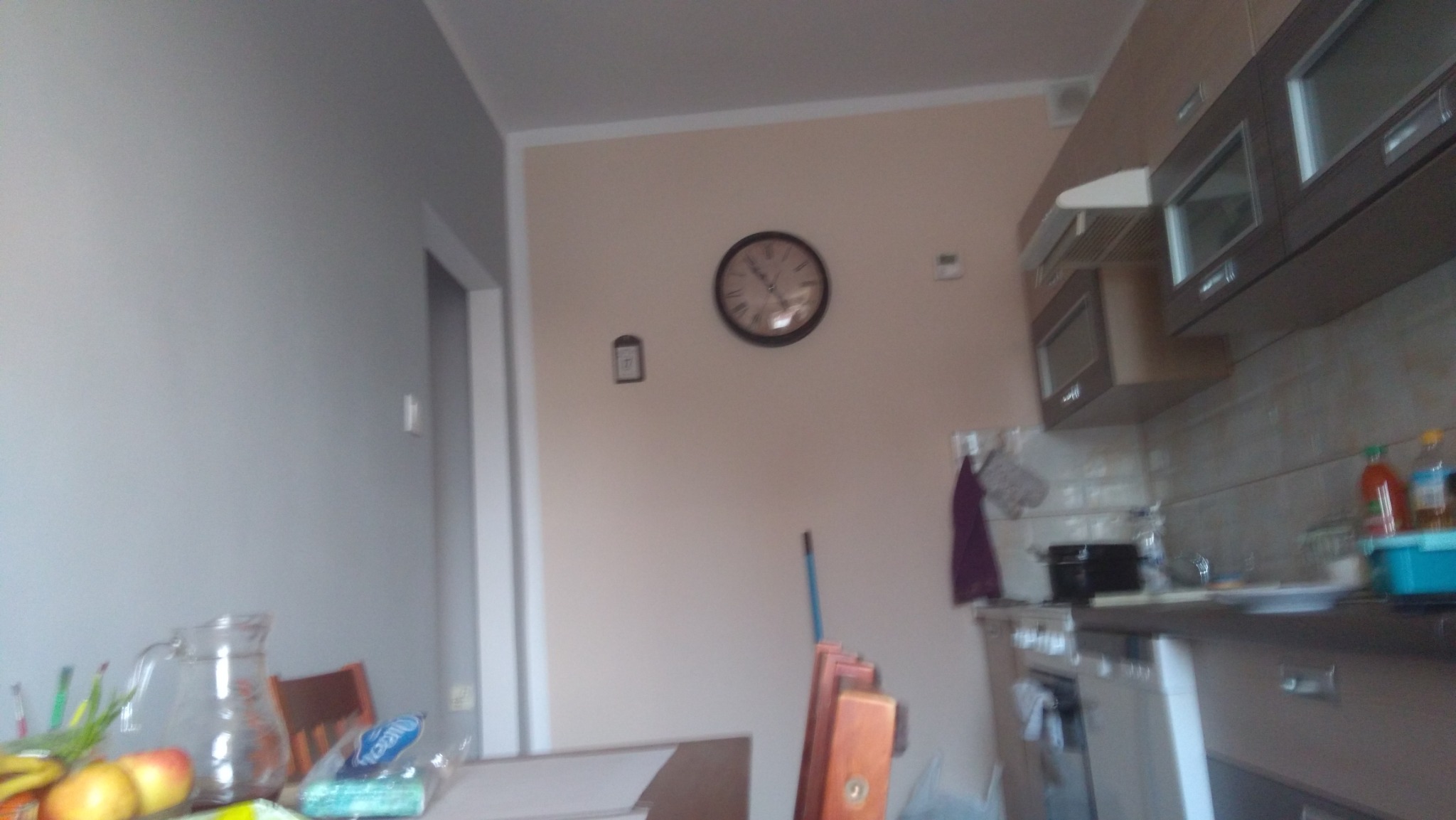Fragment kuchni w trakcie remontu: widoczne niedokończone prace, ściany w dwóch kolorach, meble kuchenne częściowo zamontowane, na ścianie wisi zegar.