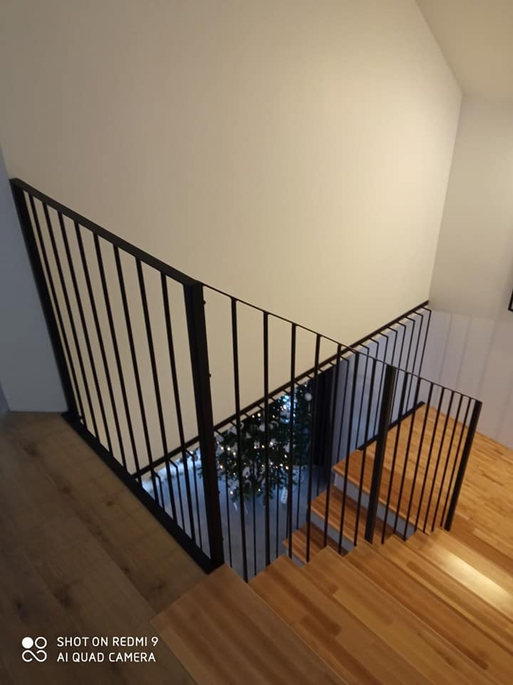 Czarna balustrada wewnętrzna z pionowymi prętami zabezpieczająca schody drewniane w domu w Sobótce, widok z góry z perspektywy pierwszego piętra na choinkę stojącą na parterze.