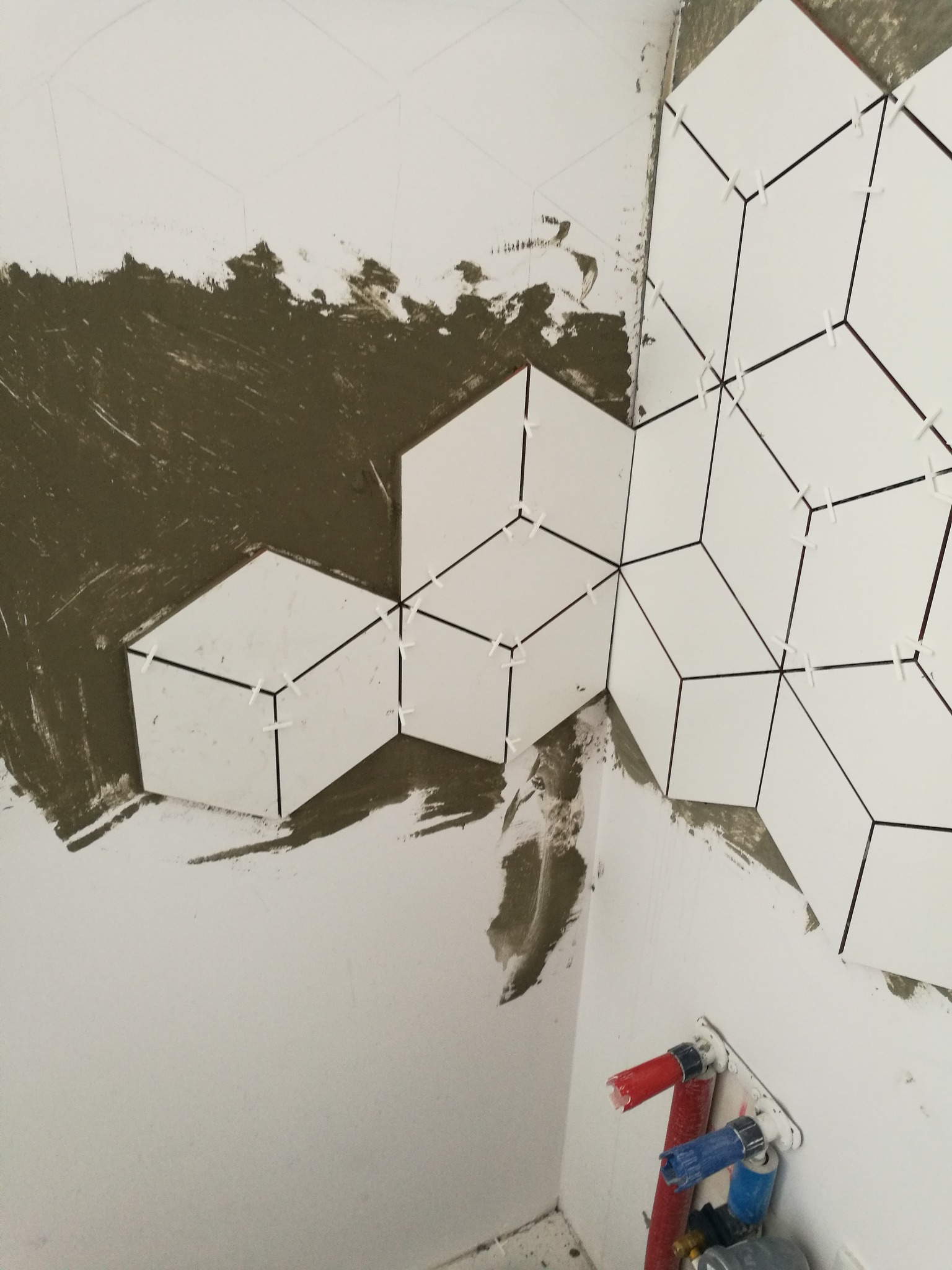 Układanie heksagonalnych płytek na ścianie w Gdyni, widoczne krzyżyki dystansowe i fragment instalacji hydraulicznej.