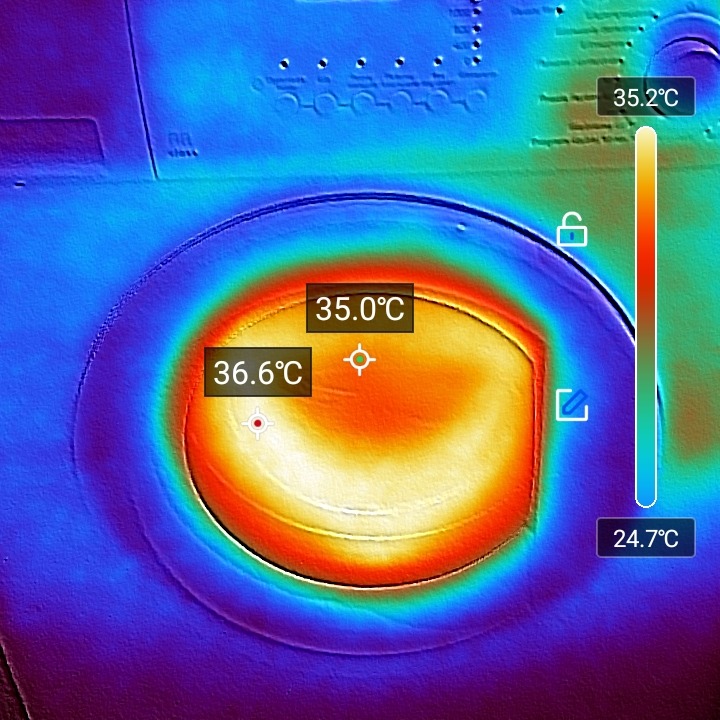 Termowizja drzwiczek pralki, ukazująca rozkład temperatur. Kolory od niebieskiego (chłodny) do czerwonego (ciepły). Widoczne wartości temperatur w stopniach Celsjusza.
