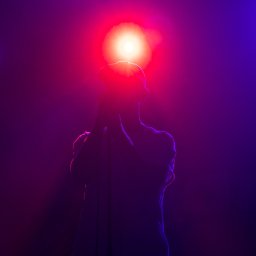Paweł Woliński - Sylwetka piosenkarza z mikrofonem na scenie oświetlonej czerwono-fioletowymi światłami.