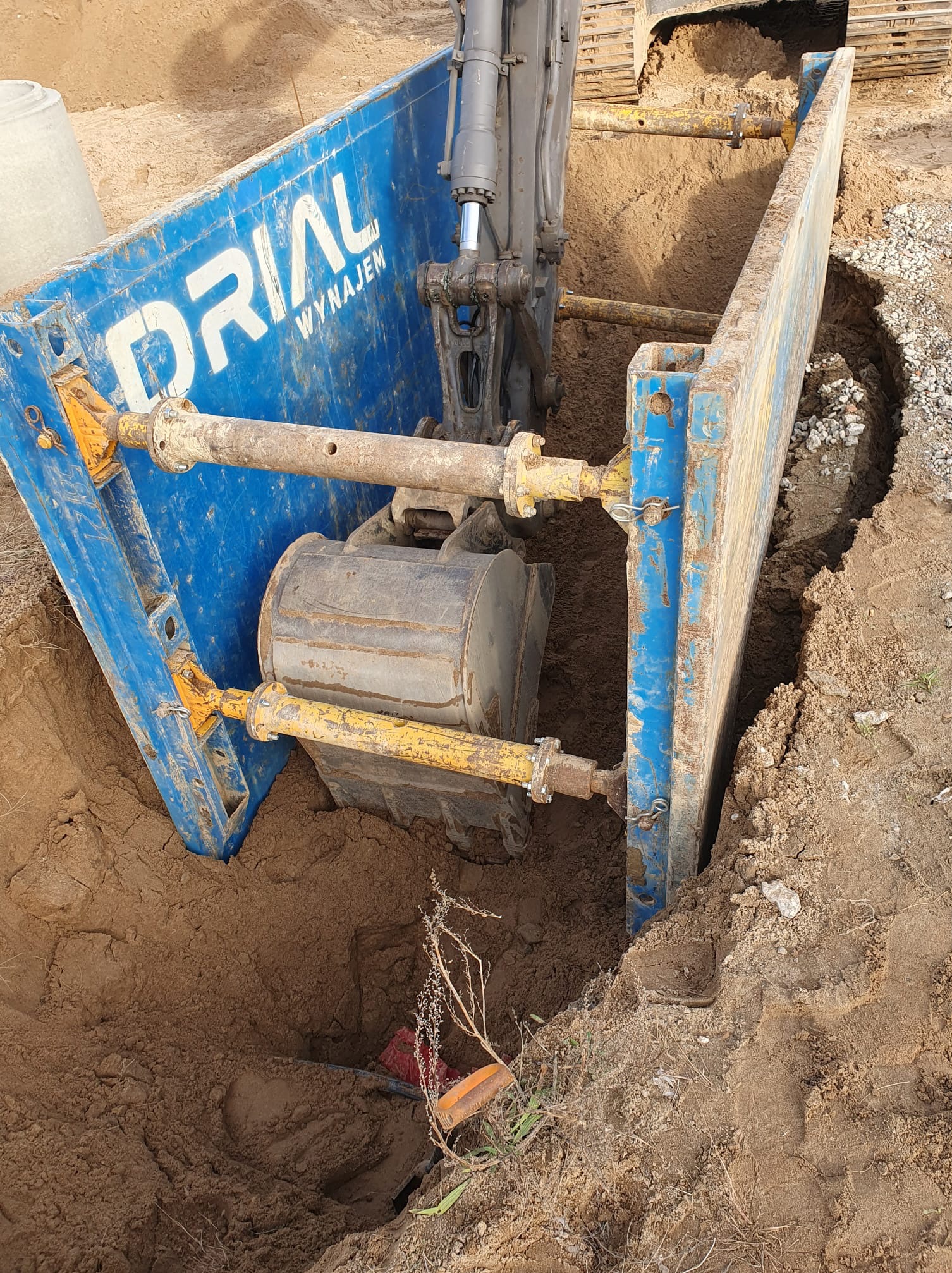 Wykonanie wykopu pod przyłącze wodno-kanalizacyjne z użyciem szalunków wykopowych, widoczne ślady pracy koparki i rury w wykopie.