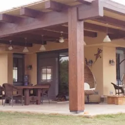 Zadaszony taras z drewnianą konstrukcją nośną, wyposażony w st&oacute;ł z krzesłami, wiszące fotele typu kokon i oświetlenie. Na ścianie budynku widoczna dekoracja w kształcie jaszczurki.