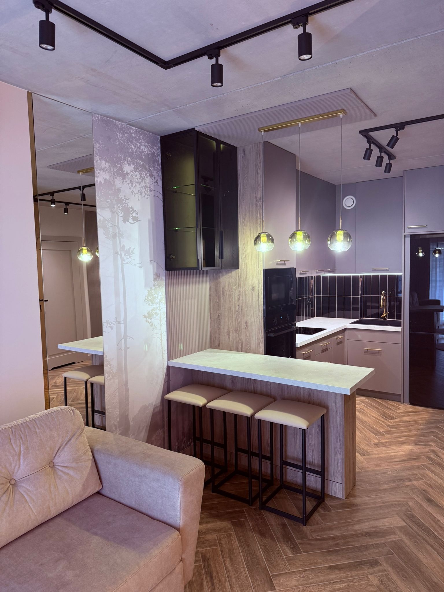 Nowoczesna kuchnia z wyspą i hokerami w Kozy. Parkiet w jodełkę, oświetlenie punktowe i wiszące lampy. Lustro powiększa przestrzeń. Minimalistyczny design.