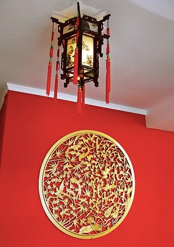 Wnętrze z czerwonymi ścianami, zdobionym złotym okręgiem z motywami roślinnymi i ptasimi oraz orientalną lampą z czerwonymi frędzlami.