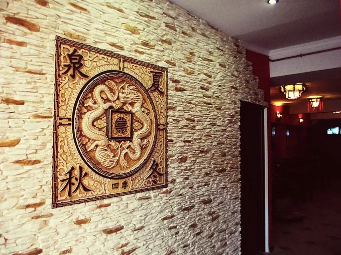 Ściana wykończona dekoracyjnym kamieniem z orientalnym płaskorzeźbą przedstawiającą dwa smoki, widok z boku.