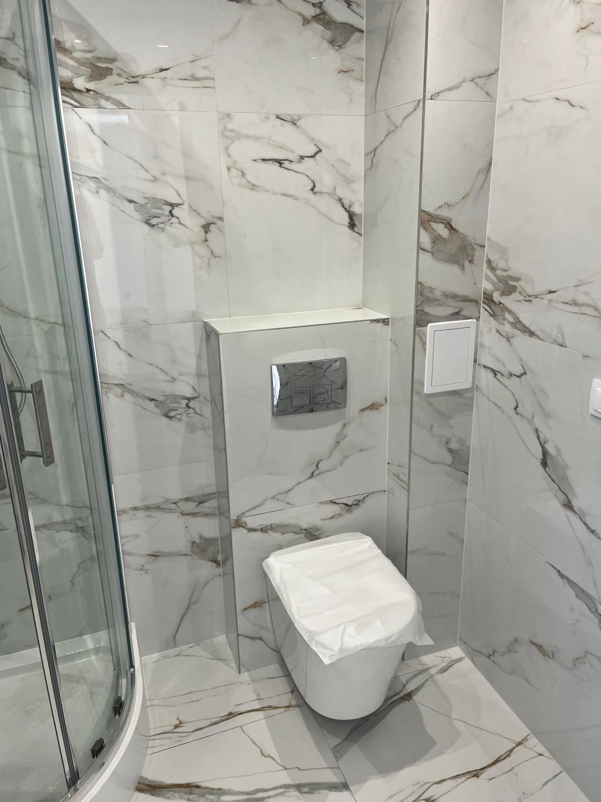 Wykończona łazienka z marmurowymi płytkami, widoczna kabina prysznicowa i toaleta zabezpieczona folią. Nowoczesny design z dbałością o detale.