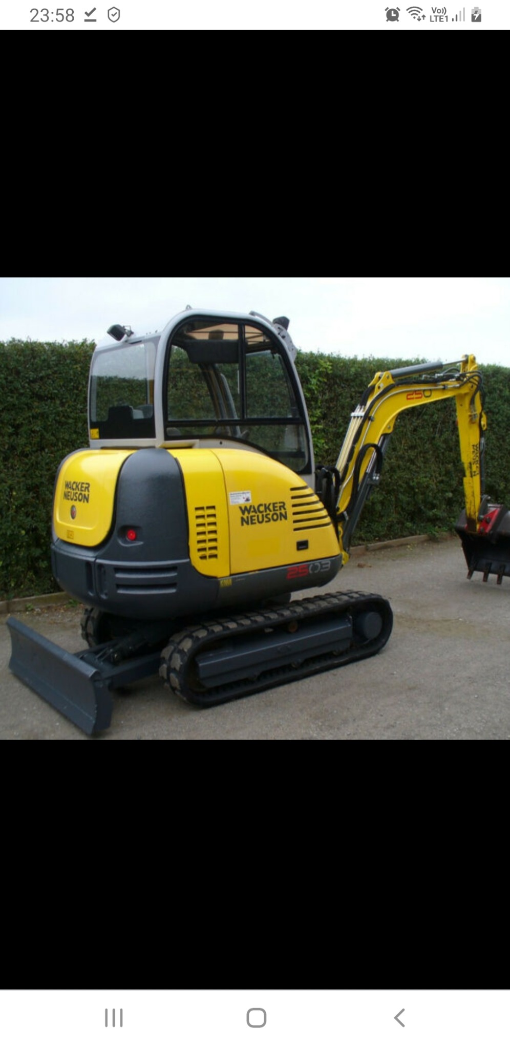 Żółto-szara minikoparka Wacker Neuson 2503 na gąsienicach, zaparkowana na betonowej nawierzchni, z zielonym żywopłotem w tle.