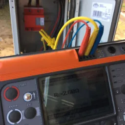 Pomiar rezystancji uziemienia za pomocą miernika MPI-530; widoczna skrzynka z zabezpieczeniem i kolorowe przewody pomiarowe.